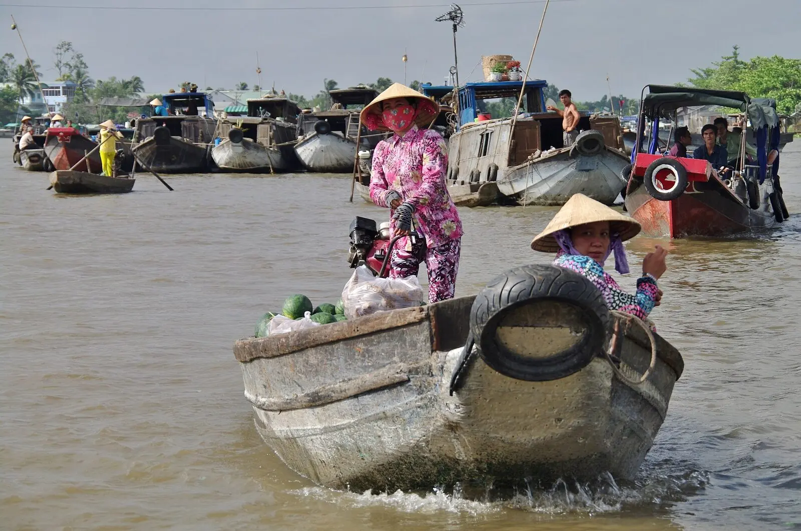 A vendor in a conical hat steering a laden boat at Cái Răng floating market, Cần Thơ